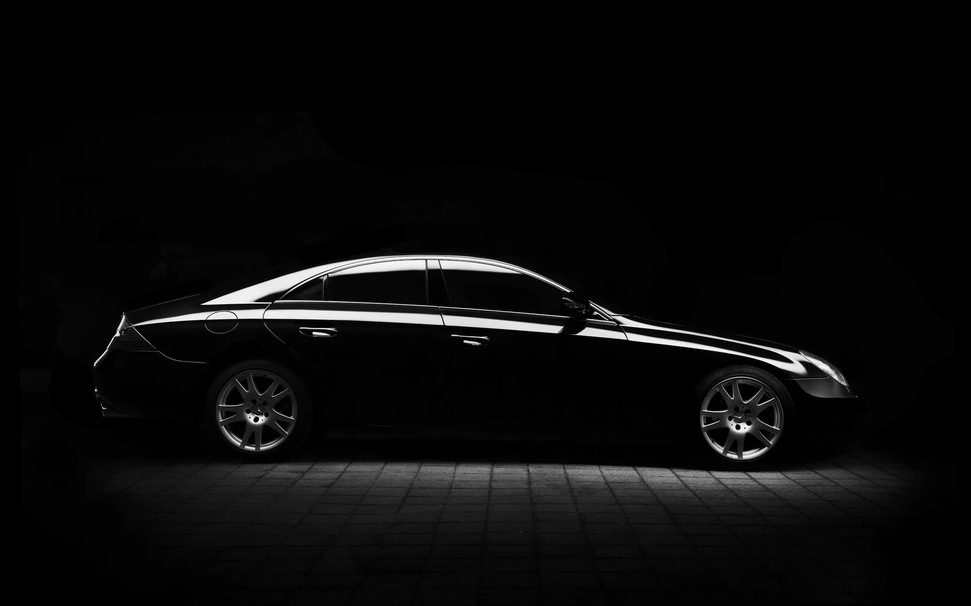 Black sedan with gloss paint lit from above in a dark studio