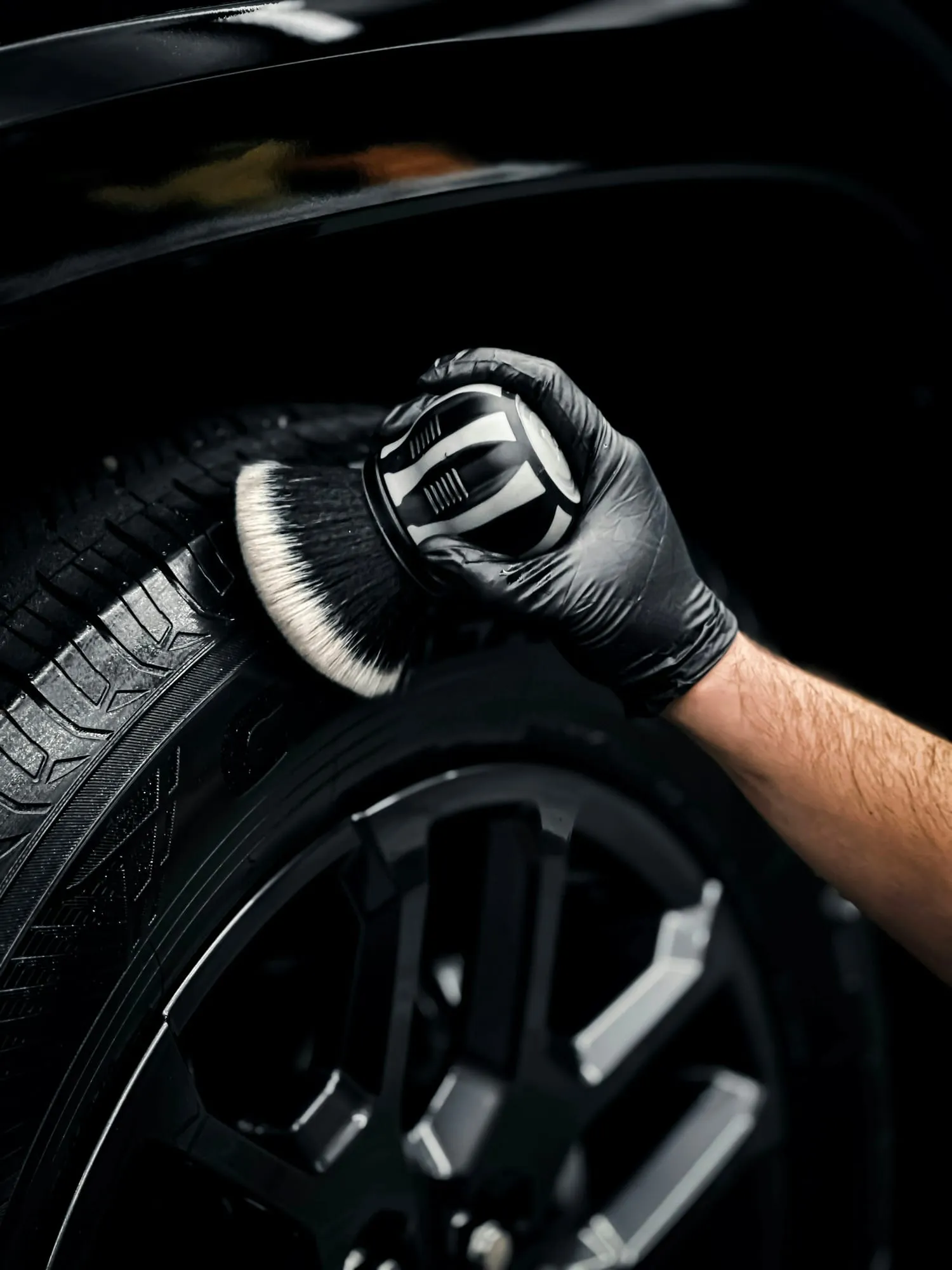 Gloved hand cleaning a tire with a soft brush
